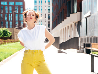 Young beautiful smiling hipster woman in trendy summer yellow jeans clothes. Carefree teen model posing in the street at sunset. Positive female outdoors. Cheerful and happy. Makes duck face, kiss