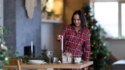 a young beautiful girl in pajamas sets the Christmas table. Puts glasses on the table. Christmas table setting.