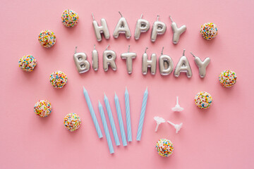 Top view of candles in shape of Happy Birthday lettering near candies on pink background.