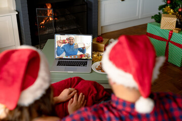 Caucasian couple with santa hats having christmas laptop video call with happy biracial man - Powered by Adobe