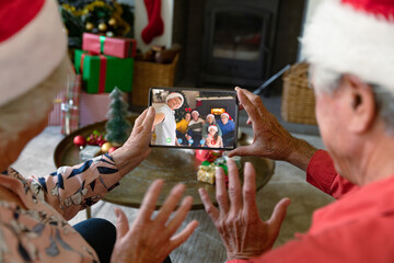 Senior caucasian couple with santa hats having christmas video call with happy caucasian family