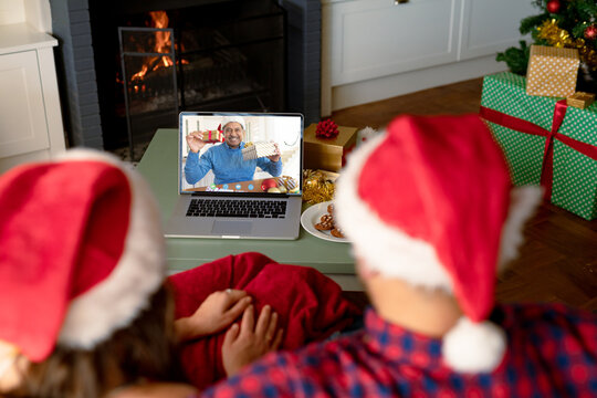 Caucasian couple with santa hats having christmas laptop video call with happy biracial man