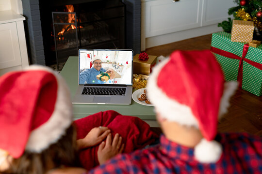 Caucasian couple with santa hats having christmas laptop video call with happy biracial man