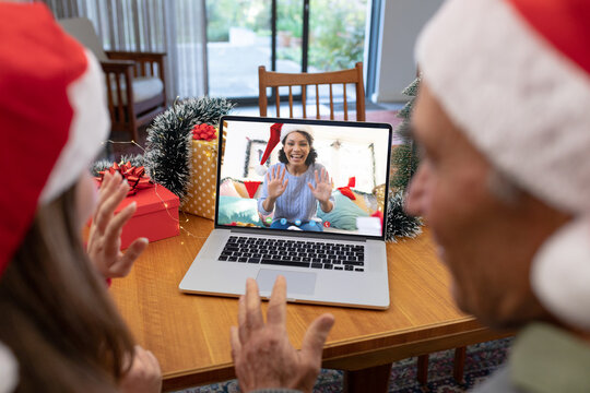 Caucasian couple with santa hats having christmas laptop video call with happy biracial woman