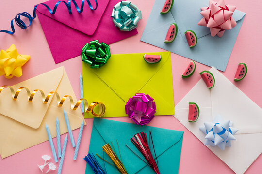 Top view of colorful envelopes near candies and serpentine on pink background.