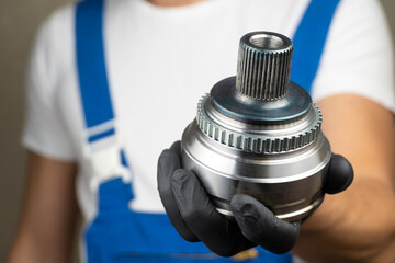 Auto mechanic in blue jumpsuit holds in his hands hinge of equal angular velocities of car and...