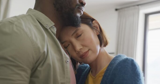 Video of happy diverse couple embracing with eyes closed and smiling at each other at home