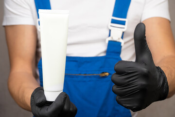 Obraz premium Close up employee in blue uniform and white T-shirt holds white tube on which you can place logo or text. Space for copying.