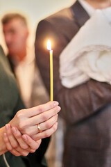 A woman holds a burning candle in her hands during a religious service.