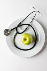 Vertical composition of stethoscope and apple on plate, on white background with copy space