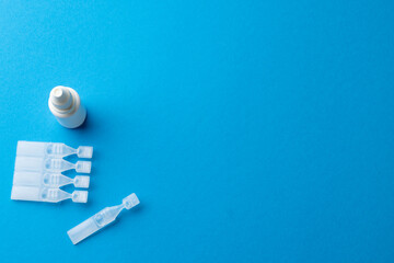 Overhead of saline solution caplets and dropper bottle on blue background with copy space