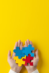 Vertical composition of hands holding jigsaw puzzle pieces on yellow background with copy space