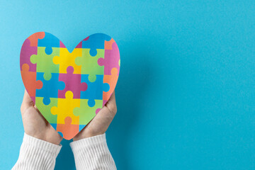 Composition of hands holding jigsaw puzzle heart on blue background with copy space