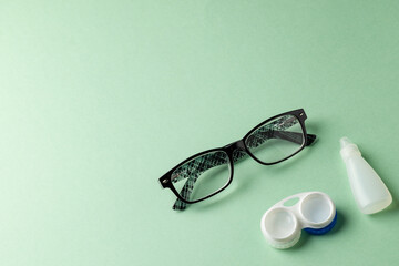 Composition of glasses with eye drops and contact lenses on green background