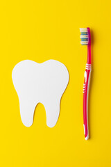 Vertical composition of white tooth and toothbrush on yellow background with copy space