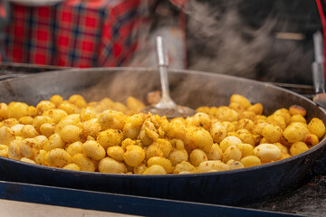 Peeled whole potatoes with small greens are cooked in a large cast-iron skillet outdoors on a city street during the Christmas and New Year's Market in Krakow. Authentic Polish culinary traditions