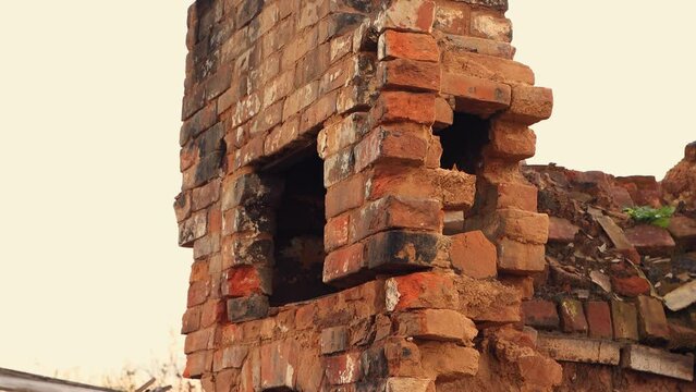 A gloomy ruined stove without a red brick chimney, the remains of a burnt house. An abandoned building, a consequence of the war, bombing, missile strikes. Ruins, people in evacuation. UHD 4K.