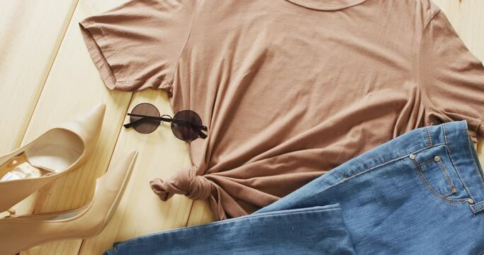 Video of close up of brown t-shirt, denim jeans and sunglasses on wooden background