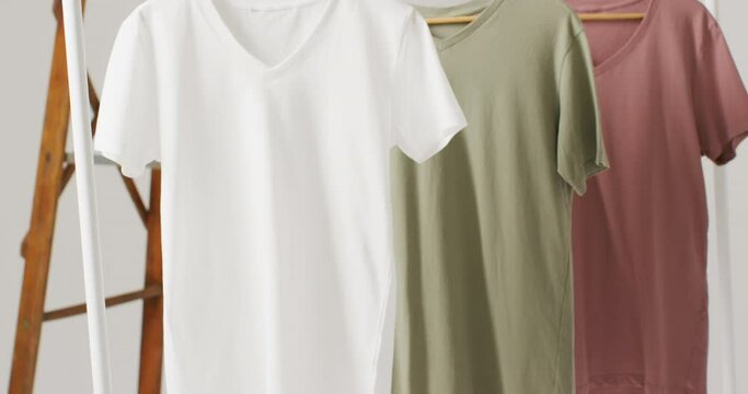 Video of close up of white, beige and gren t shirts hanging on white background