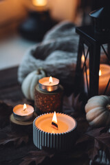 Cozy autumn composition with aromatic candle, pumpkins, wool sweater, leaves, cinnamon. Aromatherapy on a grey fall morning, home atmosphere of cosiness and relax. Wooden background close up.