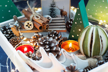 Handmade Christmas decorations, garland, candles and cones in wooden tray on blue linen tablecloth. Mood winter. Cozy home concept. Selective focus. Close up.