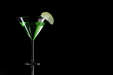 Green appletini cocktail with apple garnish in martini glass on black background