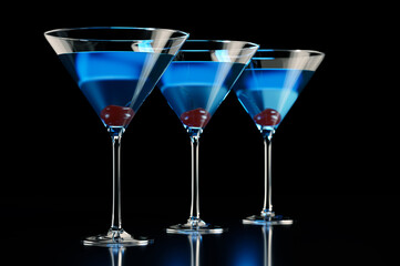 Three blue cocktails with cherry on black background