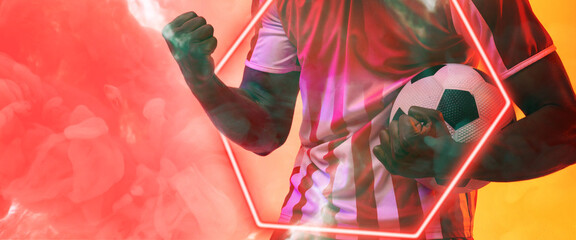 Midsection of african american male player holding ball by illuminated hexagon over smoky background