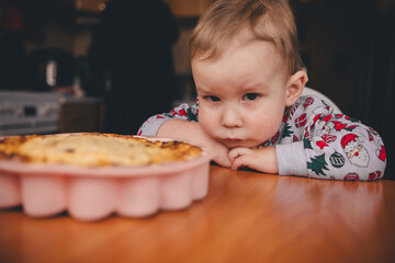 a sad child in a Christmas sweater at the home table in front of a pie