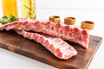 front view of juicy raw pork ribs on a cutting board. white background. spices for grilling ribs.