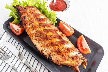 juicy grilled ribs on a ceramic dark tray with tomatoes and lettuce. tomato sauce in a bowl, to improve the taste. close angle.