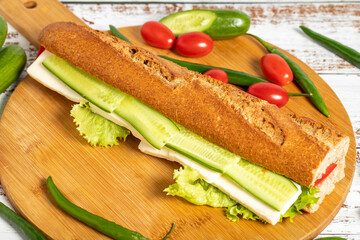 Baguette sandwich. Sandwich with olives, lettuce, tomato, cucumber, cheddar and feta cheese on wooden background