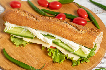 Baguette sandwich. Sandwich with olives, lettuce, tomato, cucumber, cheddar and string cheese on wooden background