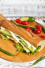 Baguette sandwich. Sandwich with olives, lettuce, tomato, cucumber, cheddar and string cheese on wooden background
