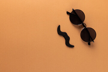 Composition of fake moustache and glasses on orange background with copy space
