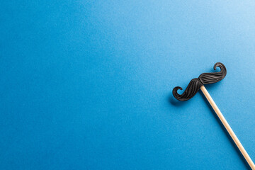 Composition of fake moustache on stick on blue background with copy space