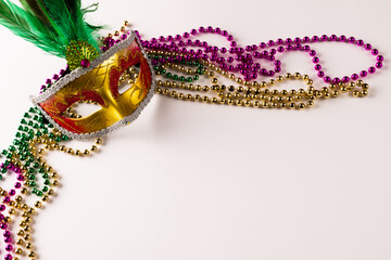 Composition of colourful mardi gras beads and carnival mask on white background with copy space