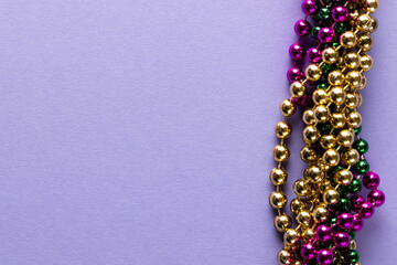 Composition of colourful mardi gras beads on lilac background with copy space