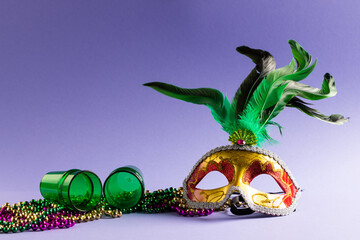 Composition of colourful mardi gras beads, shot glasses and carnival mask, on blue with copy space