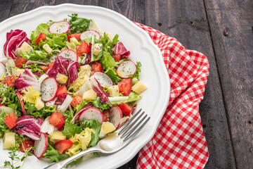 Fresh salad with mixed greens radish cheese and tomato in a plate on wooden background. Italian Mediterranean or Greek cuisine. Vegetarian vegan food.