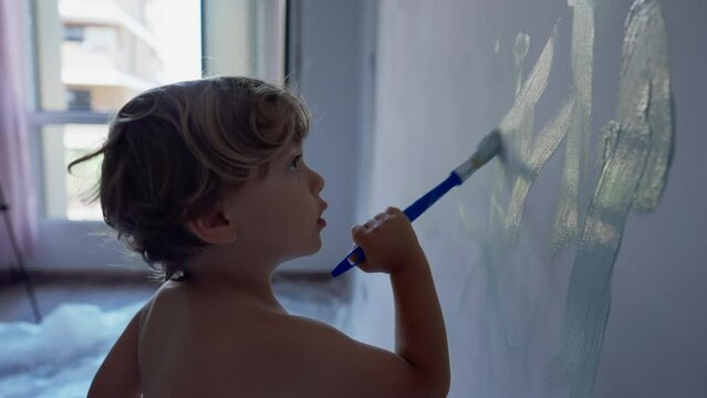 One little boy painting wall with paint brush. Child doing house renovation. Kid helping parent to paint apartment wall