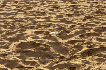 Plastic cup and footprints on a sandy beach, conceptual image