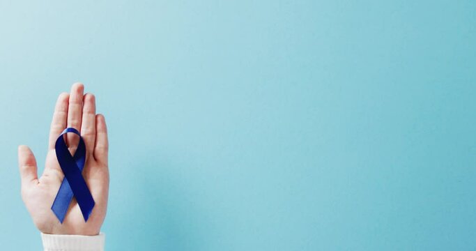 Video of hand holding blue colon cancer awareness ribbon on blue background with copy space