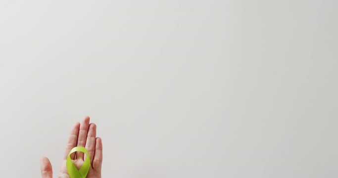 Video of hand holding pale green std awareness ribbon on white background with copy space