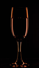 One glass of champagne in the background lighting on a black table. Silhouette of a champagne glass on a black background in a colored background