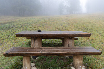 A brown wooden table with benches are outside in autumn in fog