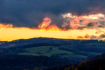 Rural evening landscape with mixed forest after sunset. Beautiful colorful sky with fiery clouds. View of the valley. Late autumn. Dubrava, Slovakia.