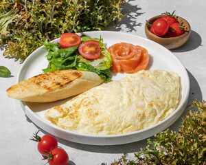 Breakfast with egg omelette with salmon, crusty bread, letucce and tomatoes on natural stone background
 