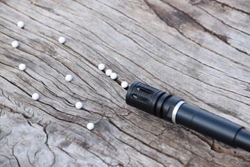 BB gun or airsoft gun muzzle and white bullets on wooden plank, soft and selective focus.