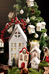 Christmas arrangement with white house shaped decors and lantern in front of Christmas tree